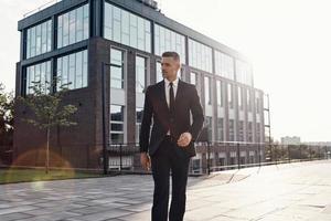 Selbstbewusster, reifer Geschäftsmann, der im Freien in der Nähe eines Bürogebäudes spazieren geht foto