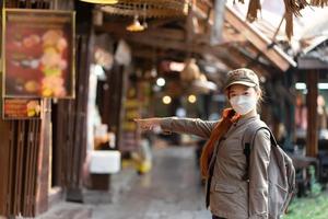 junge asiatische reisende mit maske und rucksackzeiger zum restaurant sie ist sehr hungrig foto