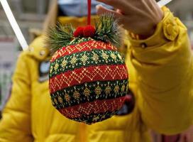 rot-grüner gestrickter weihnachtsball in der hand nahaufnahme. weihnachts- und neujahrsgeschenk, hintergrund foto