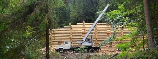 der Prozess des Baus eines Holzhauses aus Holzbalken mit zylindrischer Form. Kran in funktionstüchtigem Zustand foto