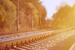 herbstliche Industrielandschaft. Eisenbahn, die sich zwischen grünen und gelben Herbstbäumen in die Ferne zurückzieht foto