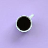 kleine weiße kaffeetasse auf texturhintergrund aus pastellviolettem modepapier in minimalem konzept foto