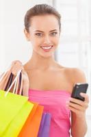 Shopaholic-Mädchen. Schöne junge Frau in rosafarbenem Kleid, die Einkaufstüten hält und am Handy spricht foto