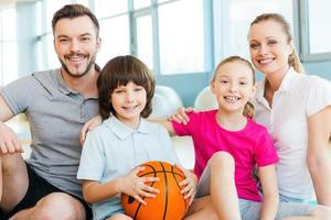 glücklich, eine Familie zu sein. Fröhliche sportliche Familie, die sich beim gemeinsamen Sitzen im Sportverein miteinander verbindet foto