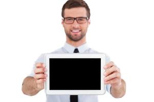 Kopieren Sie Platz auf einem digitalen Tablet. Fröhlicher junger Mann in Abendkleidung und Brille zeigt sein digitales Tablet und lächelt, während er isoliert auf weißem Hintergrund steht foto