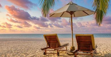 schöne tropische sonnenuntergangslandschaft zwei liegestühle, betten, regenschirm unter palmenblättern. weißer sandmeerblick mit horizont, bunter dämmerungshimmel, ruhe und entspannung. luxuriöses Strandziel foto
