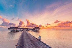 tolle Strandlandschaft. schöne Aussicht auf den Sonnenuntergang auf den Malediven. horizont bunte meer himmel wolken, über wasser villa pier weg. ruhige insellagune, tourismusreisehintergrund. exotischer Urlaub foto
