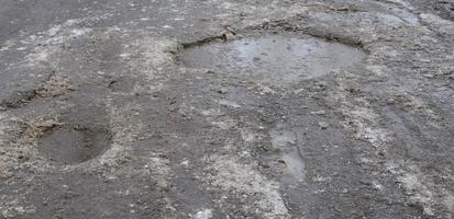 Beschädigte Asphaltstraße mit Schlaglöchern, die durch Frost- und Tauzyklen im Winter verursacht wurden. schlechte Straße foto