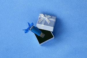 Brillantblaue USB-Flash-Speicherkarte mit blauer Schleife liegt in einer kleinen blauen Geschenkbox mit kleiner Schleife auf einer Decke aus weichem, flauschigem hellblauem Fleecestoff. klassisches weibliches Geschenk-Speicherkartendesign foto