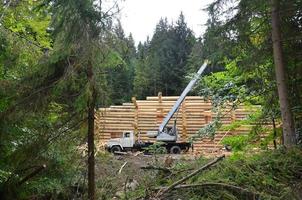 der Prozess des Baus eines Holzhauses aus Holzbalken mit zylindrischer Form. Kran in funktionstüchtigem Zustand foto