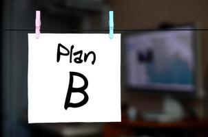 Plan B. Hinweis ist auf einem weißen Aufkleber geschrieben, der mit einer Wäscheklammer an einem Seil auf dem Hintergrund der Büroeinrichtung hängt foto