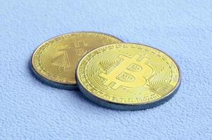 Zwei goldene Bitcoins liegen auf einer Decke aus weichem und flauschigem hellblauem Fleecestoff. physische Visualisierung der virtuellen Kryptowährung foto