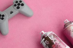 Teenager und Jugend-Lifestyle-Konzept. Joystick und zwei Spraydosen liegt auf der Decke aus flauschigem rosa Fleecestoff. Controller für Videospiele und Farbdosen auf einem Hintergrund aus Plüschvlies foto