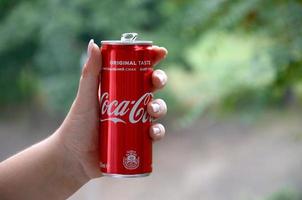 Charkow. ukraine - 2. mai 2019 kaukasische frau hält rote coca-cola-blechdose mit grünem gartenhintergrund foto