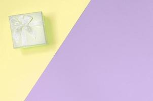 kleine gelbe geschenkbox liegen auf texturhintergrund von modepastellgelben und violetten farben foto