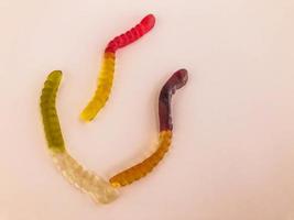 Gummiwürmer in verschiedenen Farben liegen auf einem rosafarbenen, matten Hintergrund. gallertartige Süße. blattförmige Würmer, die mit Dampf kreisen. Dekoration von Kuchen und Gebäck, Dessert für Tee und Kaffee foto