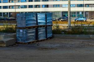 die baustelle ist vollgestopft mit material für den bau neuer häuser in der stadt. Baumaterial in transparenter Dickfolie, auf Holzpaletten, steht auf sandigem Untergrund foto