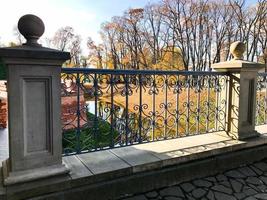 altes altes schönes schmiedeeisernes Steingeländer einer Brücke mit Mustern auf dem Hintergrund des Flusses und Bäume mit gelben Blättern foto