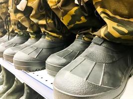 Militärische Herrengummistiefel, Schuhe in Schutzfarben Khaki Toat in einer Reihe auf dem Regal im Lager, Shop foto