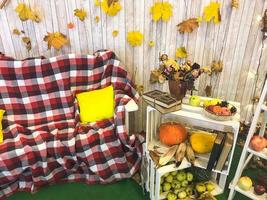 kariertes Plaid auf einem Sessel und einem Holztisch mit Vintage-Büchern, die mit Bindfäden und einer Vase gebunden sind, Herbarium, grüner Apfel auf dem Hintergrund von Holzbrettern und gelben Herbstblättern foto