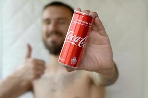 Charkow. ukraine - 2. mai 2019 lächelnder mann präsentiert alkoholfreie coca-cola-aluminiumblechdose mit ähnlichem symbol im garageninnenraum foto