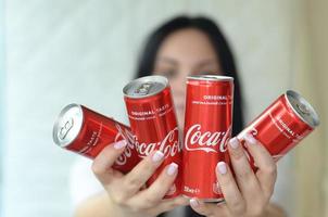 Charkow. ukraine - 2. mai 2019 glückliche frau, die viele alkoholfreie coca-cola-aluminiumblechdosen im garageninnenraum hält foto