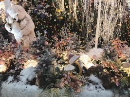 süßer, flauschiger Teddybär mit dramatischem Feenlicht und verschwommenem Weihnachtsbaum, einzeln auf schwarzem Hintergrund. urlaub, verkauf, einkaufen, motivationskonzept foto