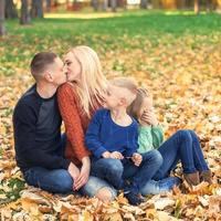 Porträt einer jungen Familie, die im Herbstlaub sitzt foto