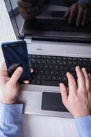 Mann hinter Laptop mit Smartphone foto