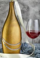 Silberkette auf goldener Flasche und Glas Wein foto