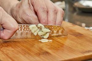 Küchenchef schneidet Knoblauch auf einem Holzbrett in der Küche foto