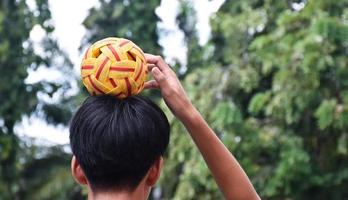 Junger südostasiatischer männlicher Sepak-Takraw-Spieler, der mit seiner rechten Hand den Ball auf dem Kopf hält, Sepak-Takraw-Spiel im Freien nach der Schule, weicher und selektiver Fokus auf den Ball. foto