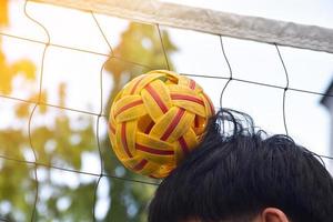 Junger südostasiatischer männlicher Sepak-Takraw-Spieler, der mit seiner rechten Hand den Ball auf dem Kopf hält, Sepak-Takraw-Spiel im Freien nach der Schule, weicher und selektiver Fokus auf den Ball. foto