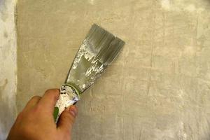 Arbeiten Sie mit einem Eisenspatel, wenn Sie die Wand mit einer Zementlösung verputzen. Reparatur der Wand mit einer Kelle mit Zement. foto