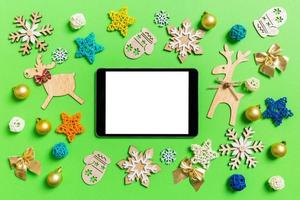 Draufsicht des digitalen Tablets auf grünem Hintergrund mit Spielzeug und Dekorationen des neuen Jahres. Weihnachtszeit-Konzept foto