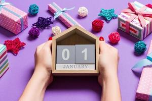 Draufsicht der weiblichen Hände, die Kalender auf purpurrotem Hintergrund halten. Der erste Januar. Feiertagsdekorationen. Neujahrskonzept foto