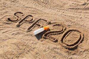 Sonnenschutzfaktor zwanzig. spf 20 wort geschrieben auf dem sand und der weißen flasche mit sonnencreme. hintergrund des hautpflegekonzepts foto
