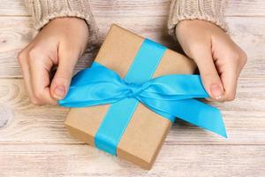 Mädchen, das eine einfache blaue Schleife auf einer Geschenkbox bindet. Eingewickelt in einfaches Bastelpapier und blaues Band. Feinschliff foto