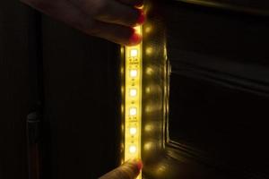 Beleuchtung installieren, der Meister macht die Installation von LED-Streifen in den oberen Nischen des Schranks zu Hause foto