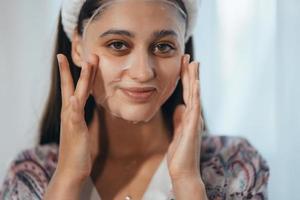 schönes Modell, das kosmetische Cremebehandlung auf ihrem Gesicht anwendet foto