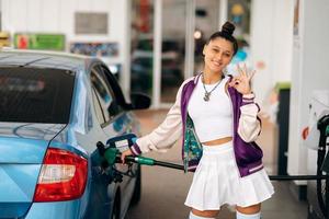 Frau, die ihr Auto an einer Tankstelle mit Kraftstoff befüllt foto