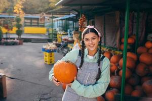 Glückliche Bäuerin in einem Jeansoverall hält reifen Kürbis foto