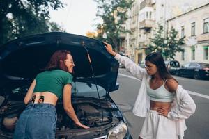 Zwei Frauen mit kaputtem Auto auf der Straße. offene Haube foto