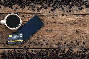 Smartphone und eine Kreditkarte, eine Tasse Kaffee und Kaffeebohnen auf dem Schreibtisch foto