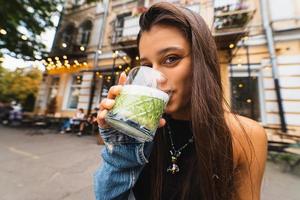 Frau, die eine Glasschale mit leckerem Smoothie hält und trinkt, im Freien foto