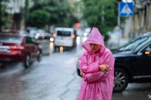 traurige Frau in einem Regenmantel auf der Straße im Regen foto