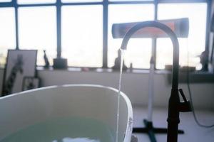 Wasser fließt aus einem luxuriösen Wasserhahn in eine große moderne Badewanne foto