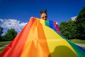 Eine junge Frau entwickelt eine Regenbogenfahne gegen den Himmel foto