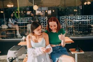 mädchen, die smartphones benutzen, während sie draußen im café sitzen foto