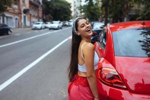 Porträt einer hübschen kaukasischen Frau, die gegen ein neues rotes Auto steht foto